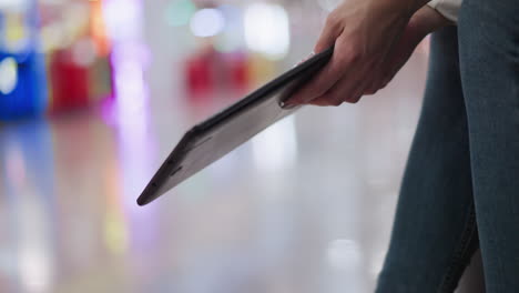 close up of hand with polished nails gently swaying tablet against vibrant blurred background featuring colorful light reflections of different shades