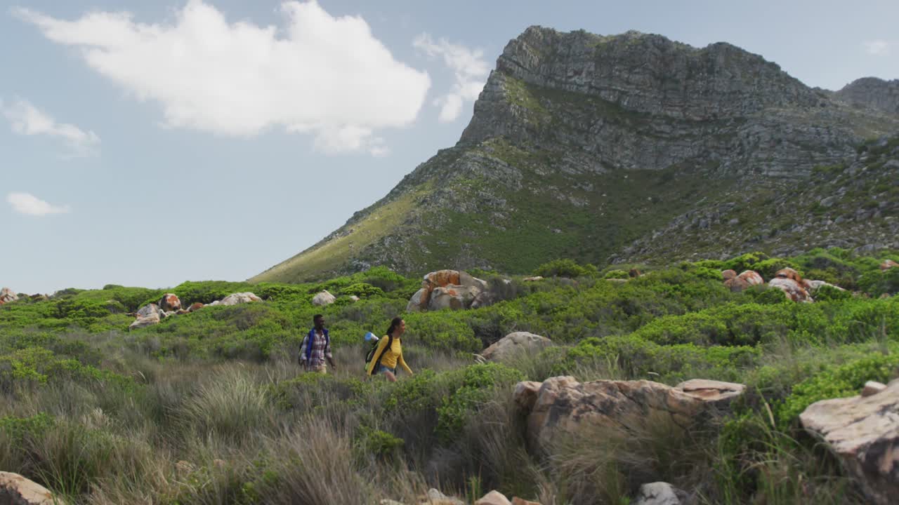 pareja afroamericana con mochilas caminando mientras caminan en las montañas