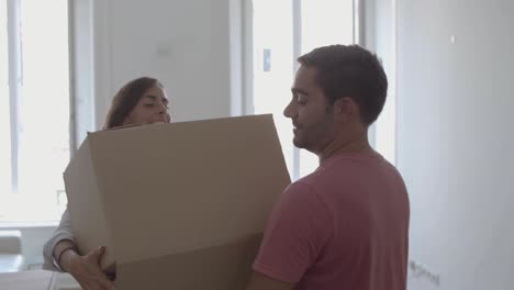 hombre feliz entrando a la habitación, cargando una caja con cosas diferentes, besando y abrazando a su joven esposa