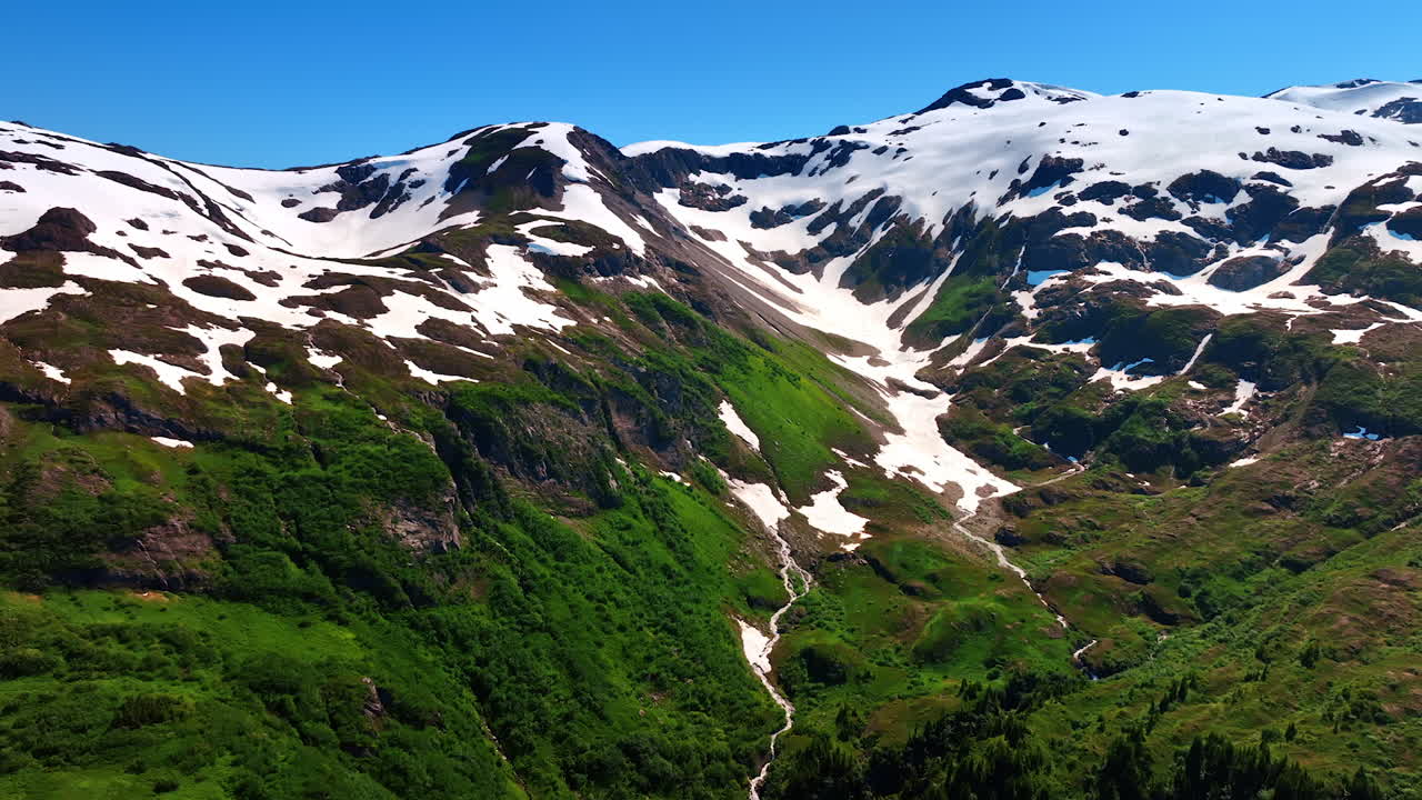 Distancing from the mountain top covered with some snow. Drone footage over the gorgeous rocks on sunny day. Alaska nature