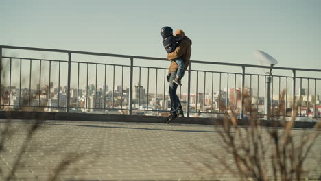 a father tenderly holds his son close to an iron railing, stepping down and then back up, both observing the cityscape below, they are both dressed jacket and beanie