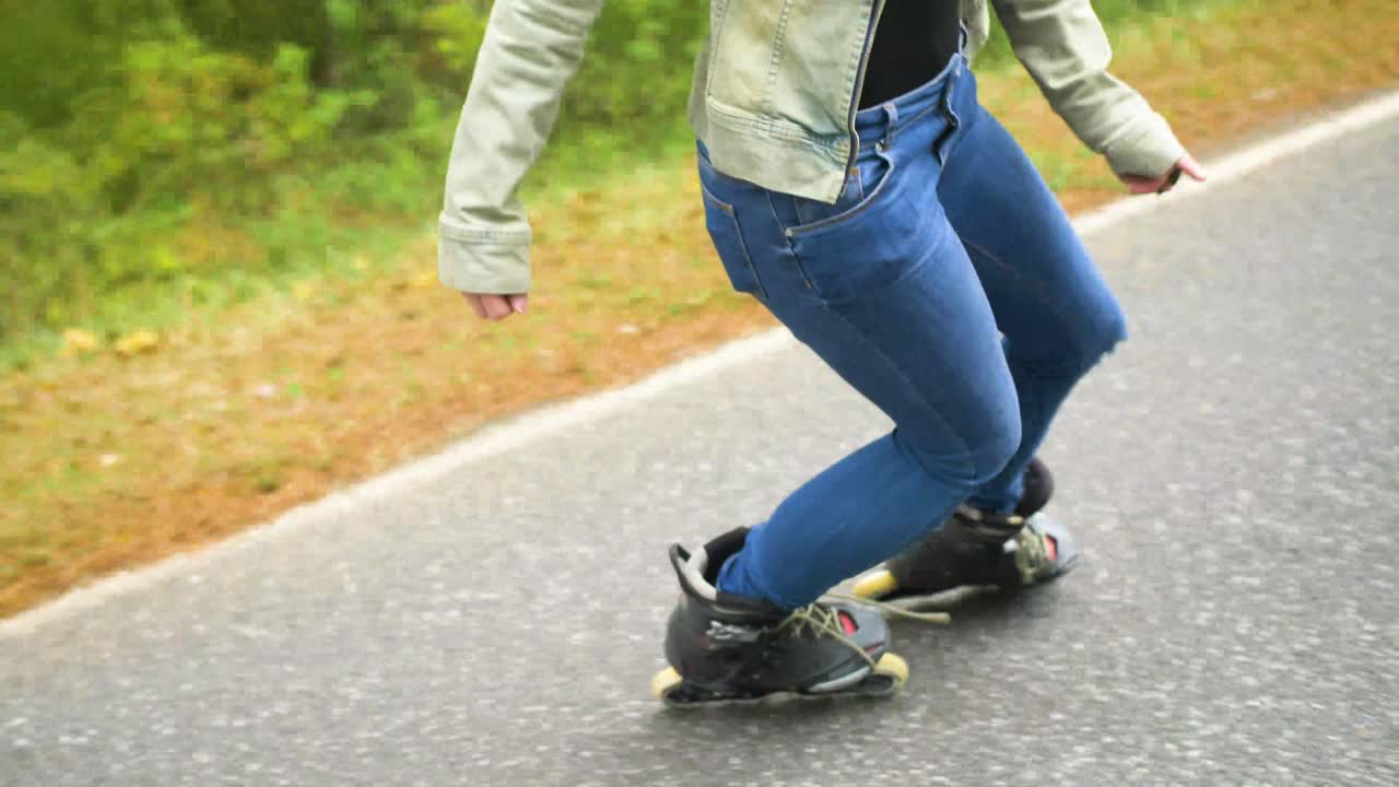 Young girl with inline skates on the street, is skating backwards. Road in the forest during the autumn day.