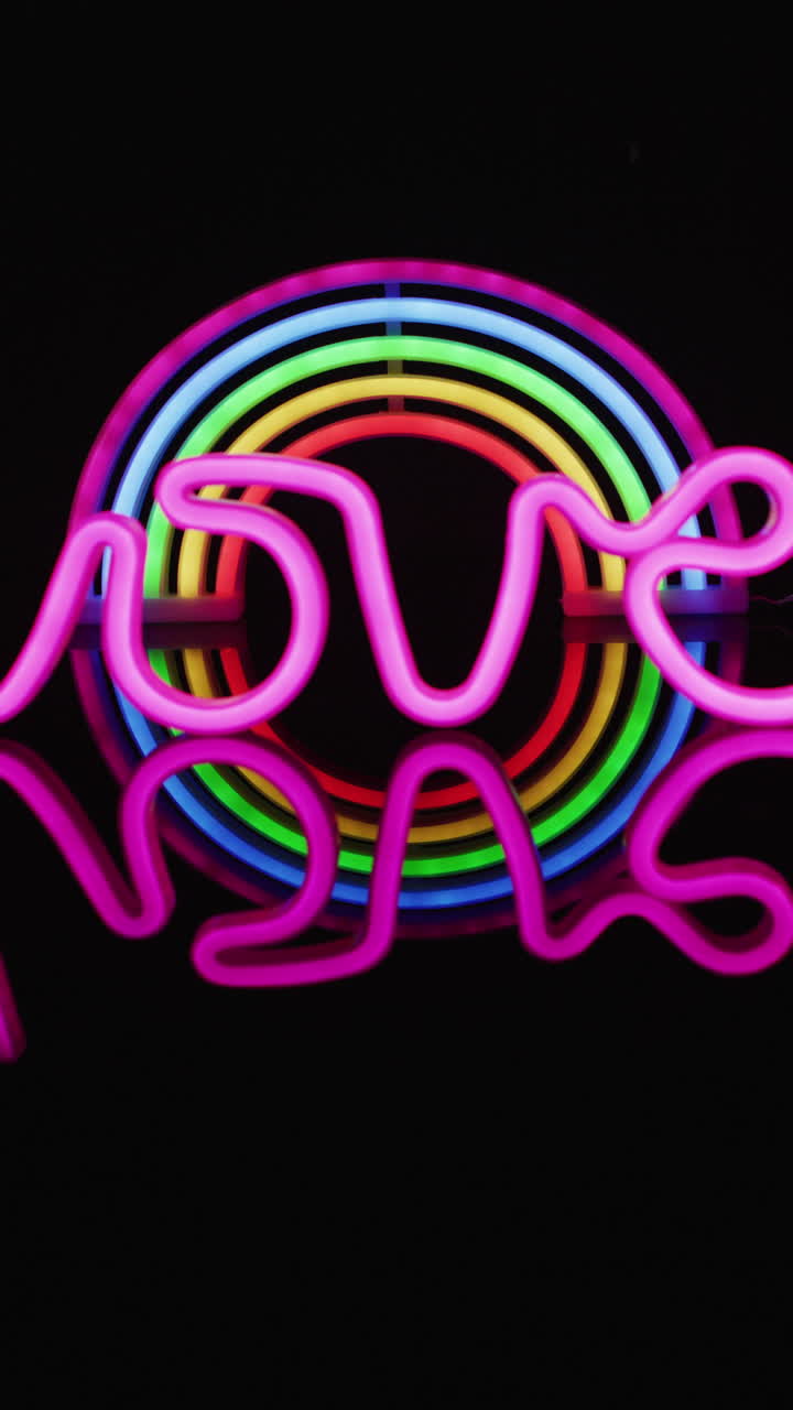 Vertical video of pink neon lights forming love text over rainbow on black background