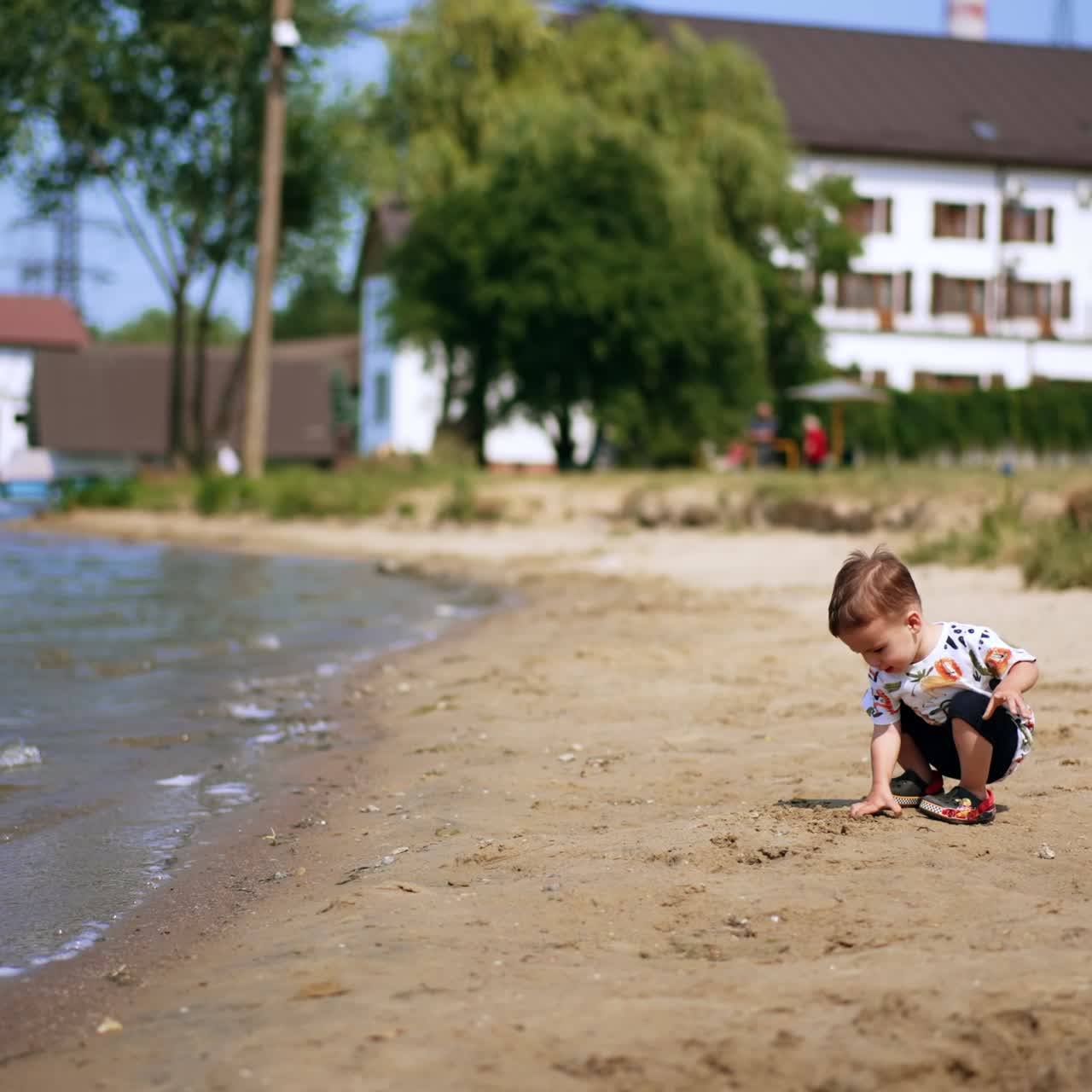 Small baby boy squatted on the lake shore. Caucasian toddler picks some sand with bare hands