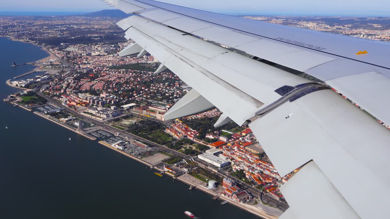 Uma cena aérea luminosa de viagem mostra a asa de uma aeronave sobre Lisboa, enquanto a malha da cidade e a costa atlântica se revelam abaixo durante uma aproximação de aterrissagem suave em um dia ensolarado. Perspectiva do céu sobre a paisagem urbana