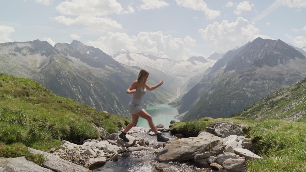 una hermosa chica rubia con un vestido blanco salta a través de un pequeño arroyo de izquierda a derecha