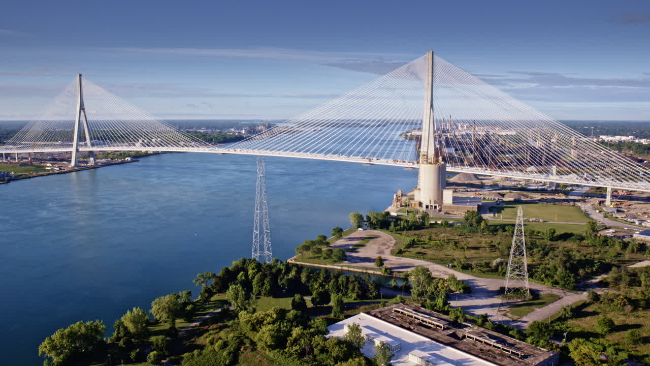 A bird's-eye view of the Gordie Howe Bridge extending into an industrial landscape by the river