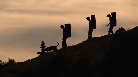 panleft of three backpackers and a dog silhouetted against an evening sky