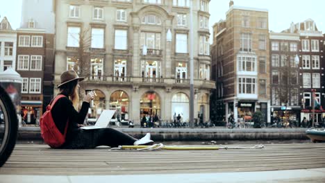 4k student girl works with laptop in the street. fashion art worker with red backpack and thermal mug. lifestyle shot