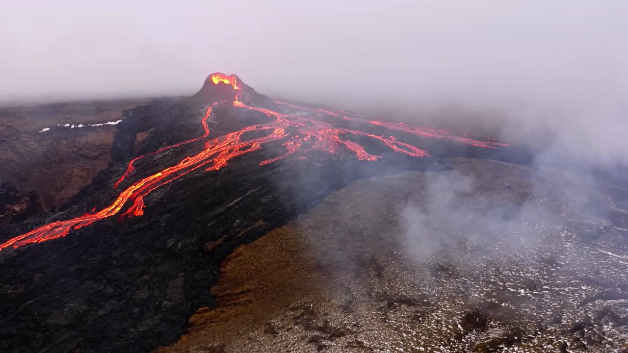 A 4K drone captures aerial cinematic shots of a volcano ejecting lava amidst a smoky environment in Iceland, presenting unique perspectives of the natural spectacle