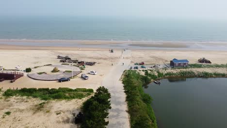 Luftbildfilm-Nach-Vorne-Dolly-Blick-Auf-Den-Strand-Von-Nanhai-Mit-Booten,-Teich-Und-Menschen,-Die-Rad-Fahren