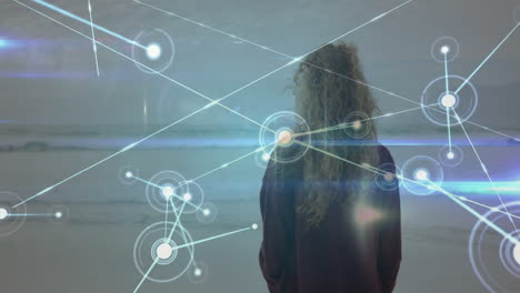Facing ocean, woman with curly hair viewing digital network animation overlay