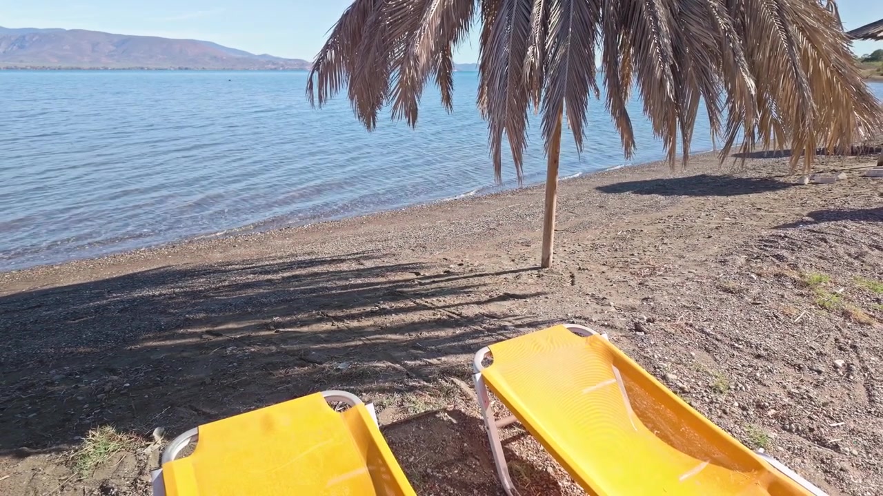 Spiaggia greca deserta con lettini prendisole e ombrelloni di palma