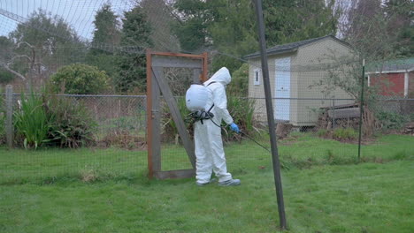 hombre vestido con equipo de protección rociando herbicida en el patio