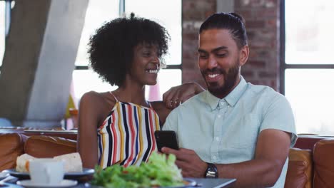 Diverse-male-and-female-colleagues-sitting-in-cafe-using-a-samrtphone-having-a-discussion