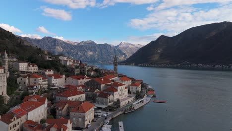 La-Toma-De-Un-Dron-En-4k-Captura-La-Encantadora-Ciudad-De-Perast,-Montenegro,-Con-Una-Hermosa-Vista-De-La-Iglesia-De-San-Nicolás,-La-Bahía-De-Kotor,-Declarada-Patrimonio-De-La-Humanidad-Por-La-Unesco,-Y-Las-Montañas-Al-Fondo