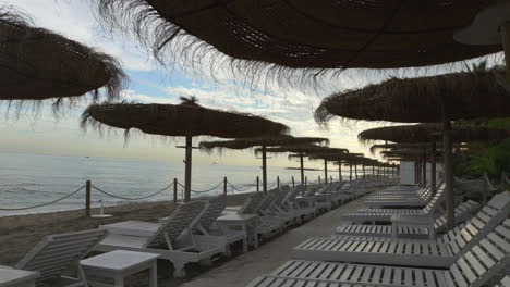 Día-De-Playa-Nublado,-Perspectiva-Desde-Tumbonas-Blancas-Y-Sombrillas-De-Paja,-Playa-De-Marbella,-Milla-Dorada