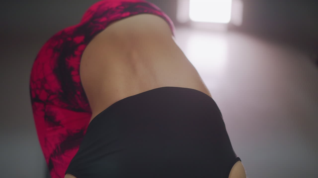 Closeup gym woman bending over mat, dynamic core activation with visible lower back and oblique engagement, red patterned leggings and black crop top, studio light flare, highenergy training