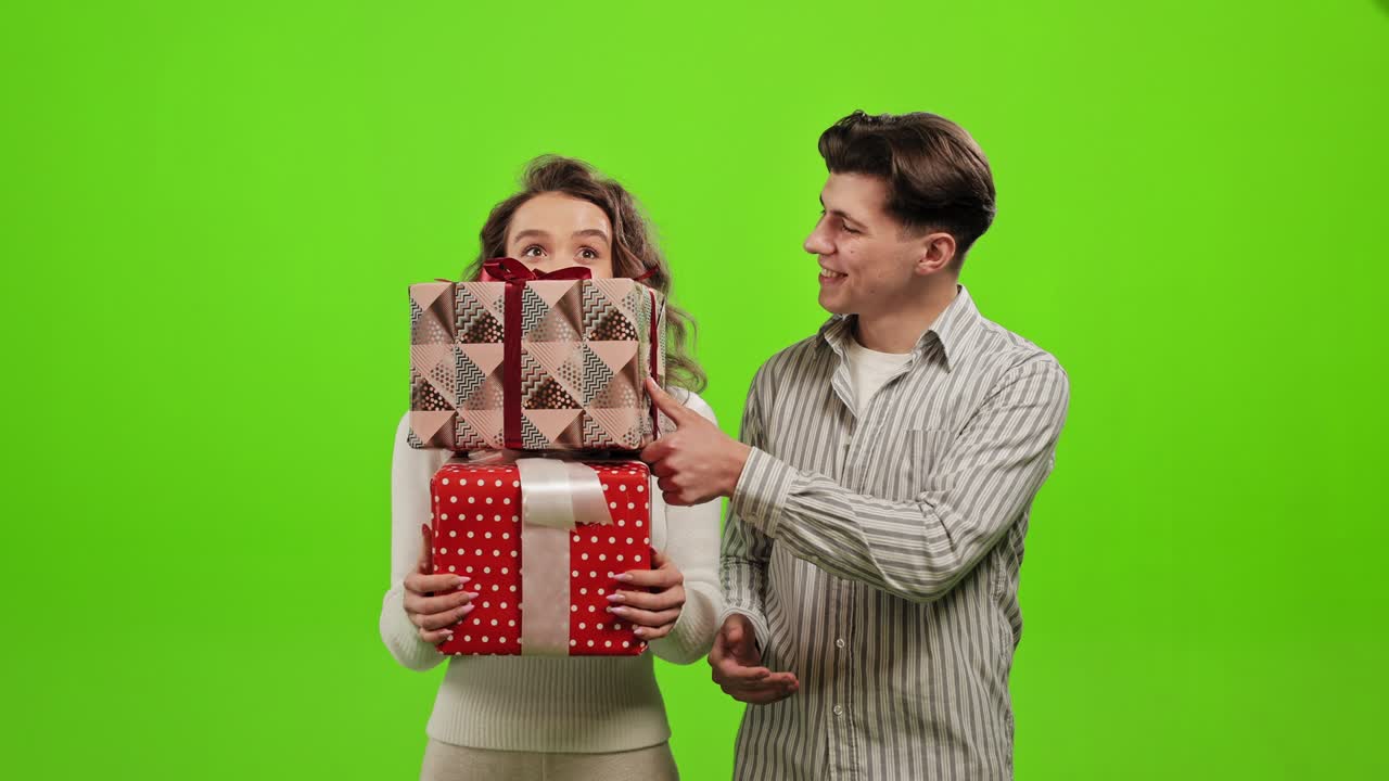 남자와 여자가 선물을 들고 있다.남자가 선물을 여자의 선물 위에 놓고 있다.여자는 행복하고 미소 짓고 있다.그들은 녹색 바탕에 서 있다.녹색 화면.