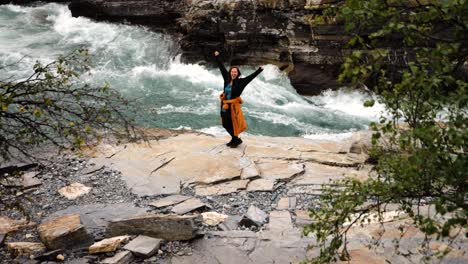 Static-shot-of-a-woman-standing-and-cheering-with-open-arms-and-her-back-on-Torne-River-inside-Aurora-Camp-Kurravaara,-Sweden