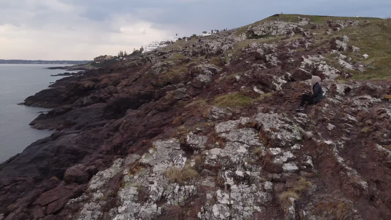 изолированная и неузнаваемая женщина сидит на скалистом утесе и смотрит на панораму морского пейзажа, пунта балена