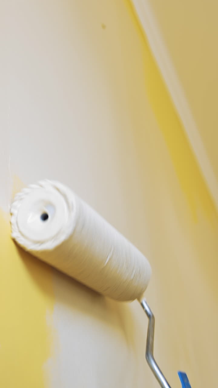 Unrecognizable worker painting wall. Paint roller with light color in man's hand moving up and down on the wall indoors. Room renovation. Close-up. Vertical video