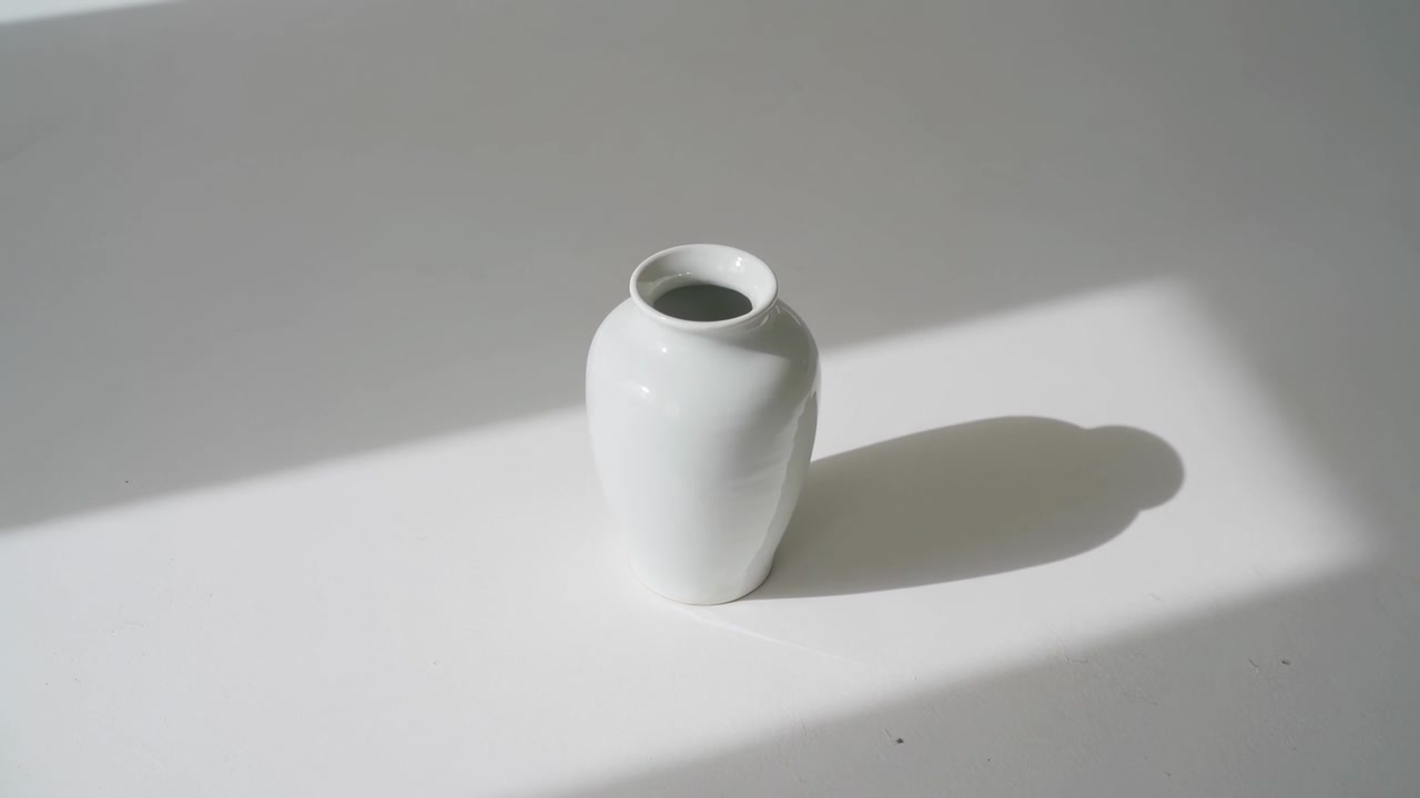 窓から差し込む光が陶器の花瓶の影を日当たりの良い長方形に落とし、影の縁を柔らかくしている。