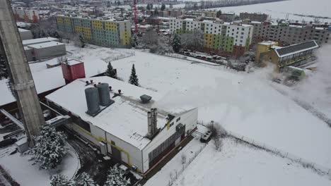 Vista-De-La-Chimenea-Humeante-De-Una-Central-Térmica-Cubierta-De-Nieve-En-Invierno,-En-El-Fondo-Casas-Y-Bloques-De-Pisos,-República-Checa