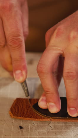 worker cuts leather belt edge with special sharp knife at workbench in studio closeup. process of handmade accessory creation. art hobby