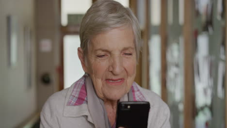 portrait of friendly elderly woman using smartphone browsing reading messages sms texting on mobile phone app in retirement home