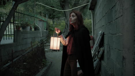 woman walks with lantern mysteriously between houses and olive trees