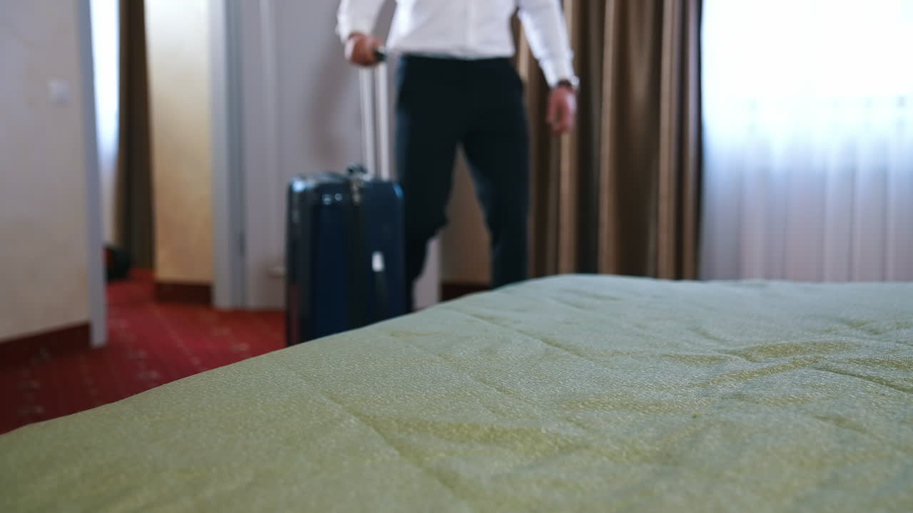 Unrecognizible businessman has just entered a hotel room and ready to unpack suitcase. Man puts luggage on a hotel bed.