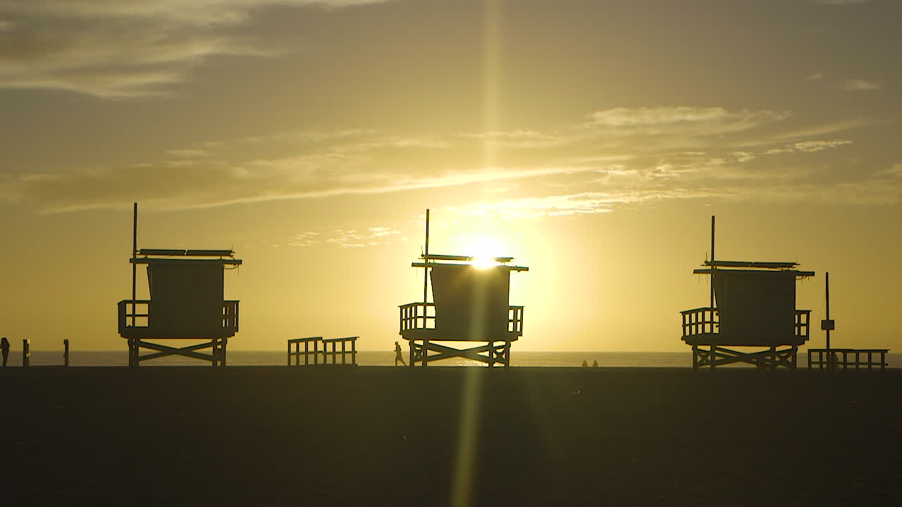 Sunset behind the lifeguard towers on Venice Beach, California. Silhouetted in slow motion.