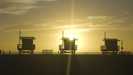 sunset behind the lifeguard towers on venice beach, california. silhouetted in slow motion.