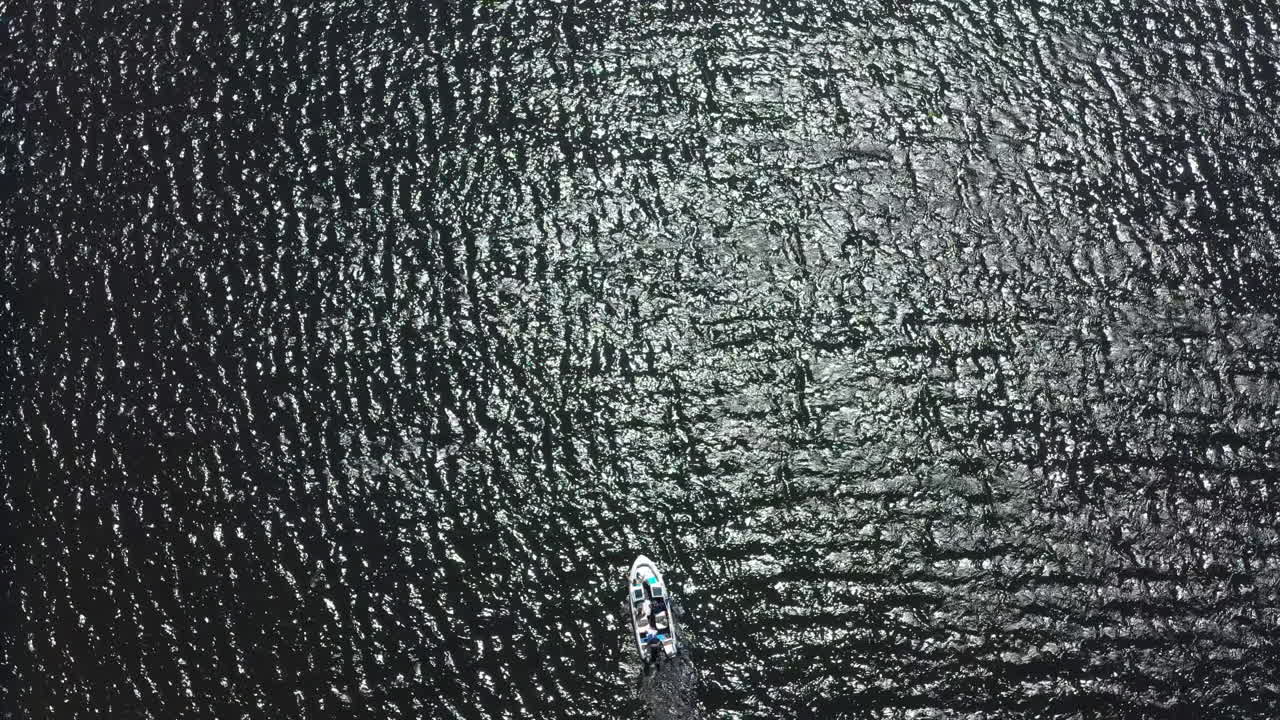 Ripresa con drone ad alta quota di una piccola barca sola in mare, con la luce del sole che splende sulla superficie dell'acqua.