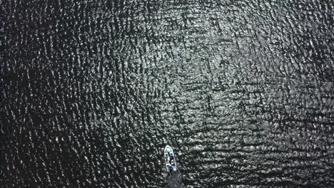 a high altitude drone shot of a small boat alone in the sea with the sunlight shine on the surface of the sea