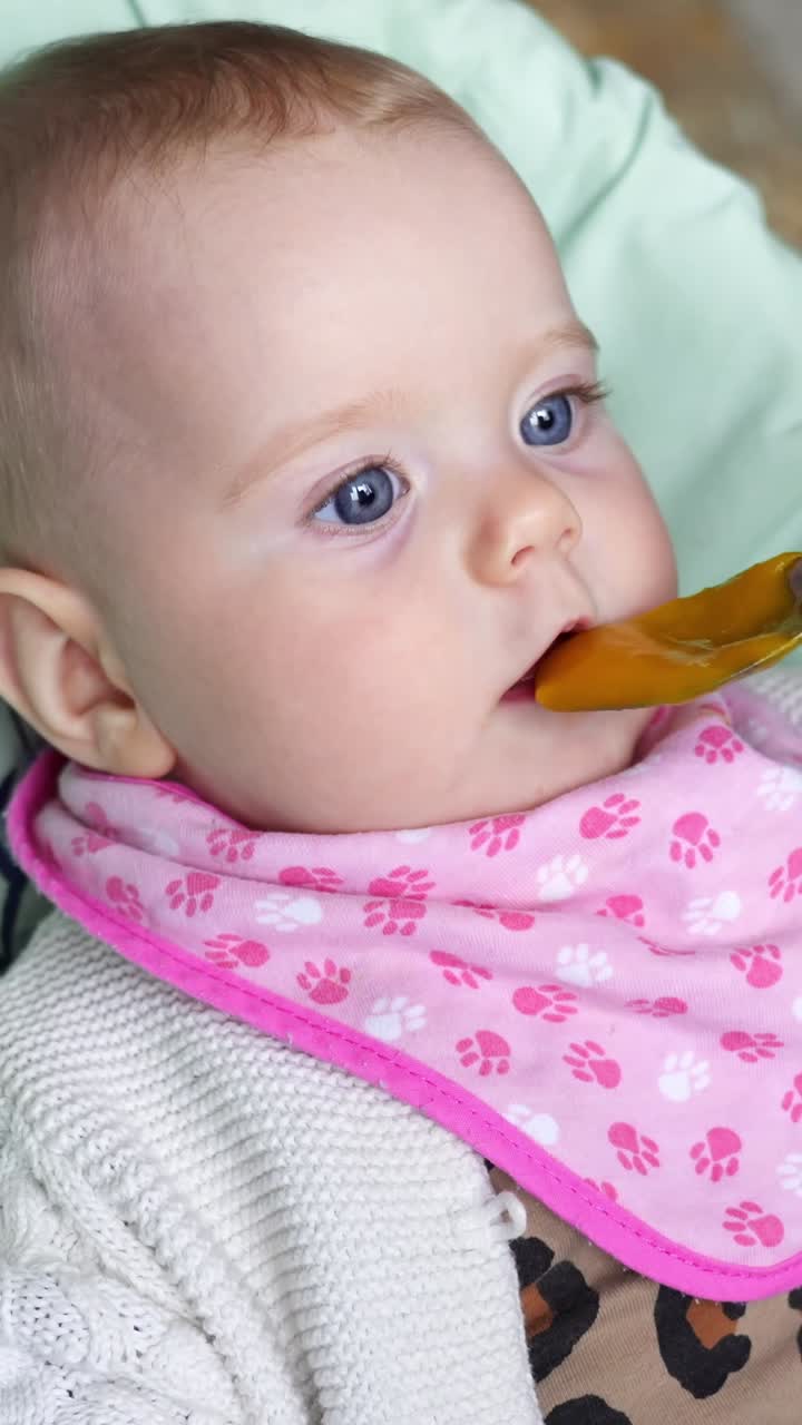 Close-up of a baby with bright blue eyes and a pink bib, opening mouth with anticipation during feeding time.