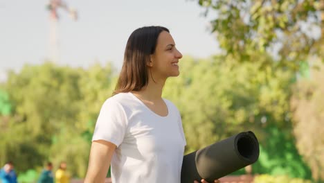chica india caminando con un tapete de yoga en un parque por la mañana
