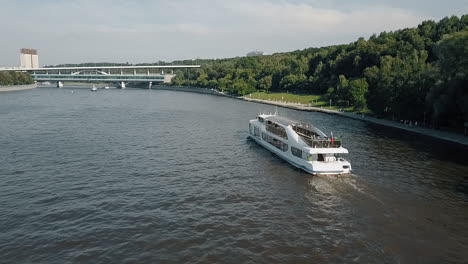 Eine-Luftaufnahme-Eines-Bootes,-Das-Sich-An-Einem-Sonnigen-Tag-Langsam-Auf-Einem-Städtischen-Fluss-Bewegt