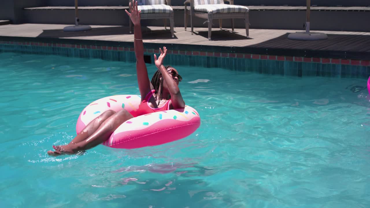 Male swimmer is tossing beach ball across pool to women on pink floats for pool play