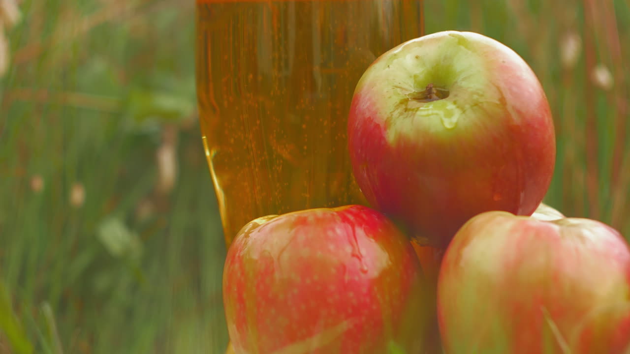 Luscious ripe apples site in front of refreshing cider pint glass in field, close-up