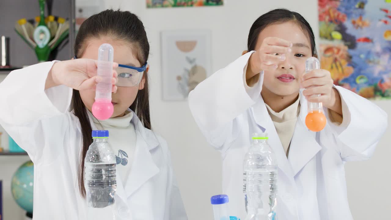 白衣を着た二人の若いアジア人少女が卓球ボールを使って物理実験を行う