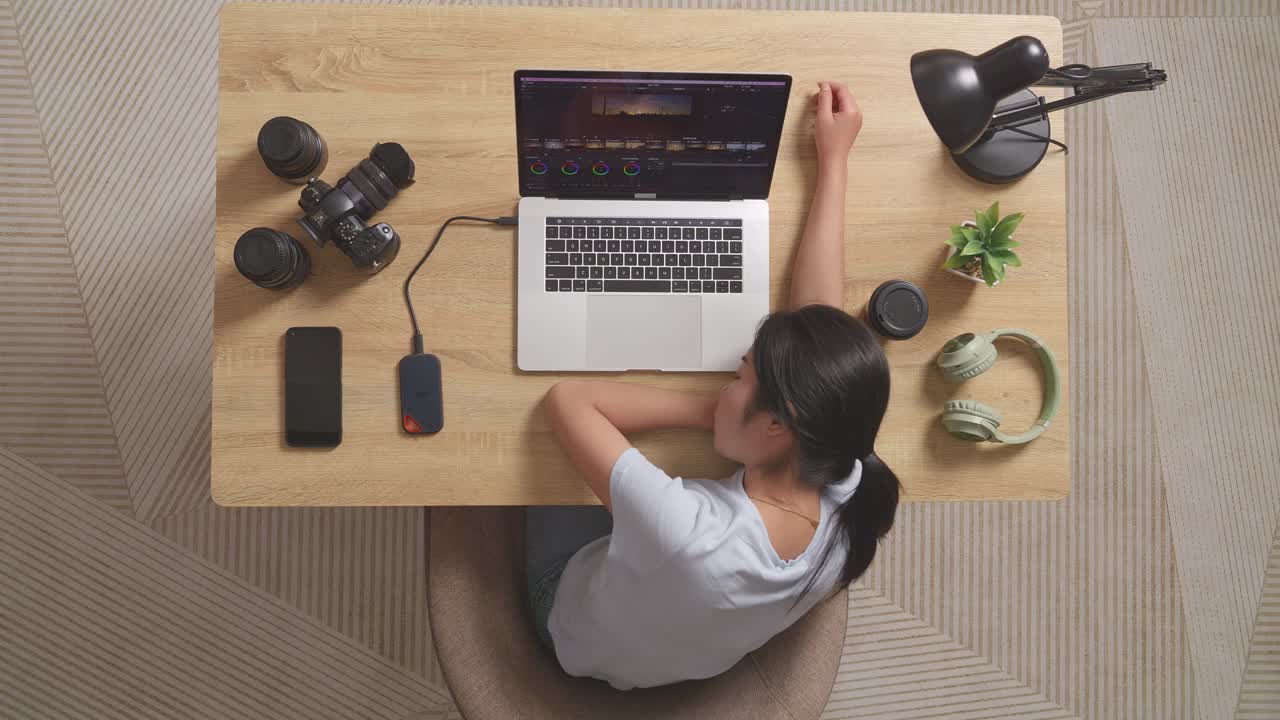 Top View Of Asian Woman Color Grading Sleeping While Sitting In The Workspace Using A Laptop Next To The Camera Editing The Video At Home