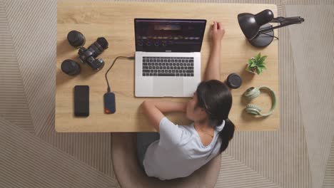 top view of asian woman color grading sleeping while sitting in the workspace using a laptop next to the camera editing the video at home