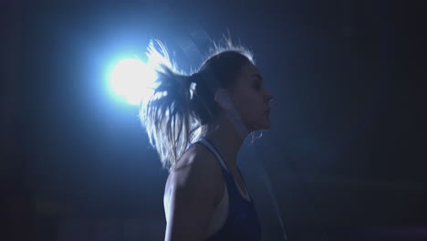 entrenamiento de cardio para luchadores. joven mujer hermosa boxeadora profesional en entrenamiento en el pasillo salta en una cuerda a la luz de la contra en una habitación oscura con ropa azul