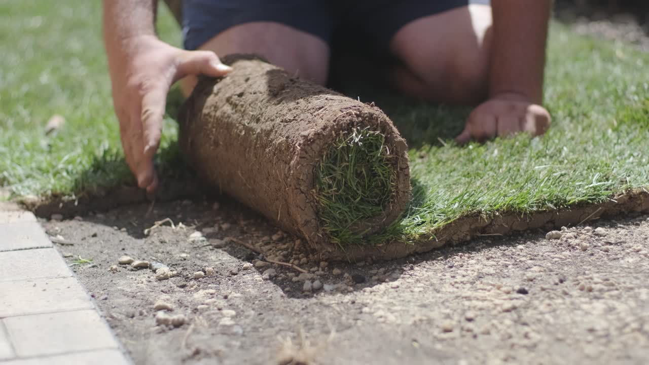Mand lægger græsruller i baghaven til plæneinstallation og haveprojekt med fokus på boligforbedring og udendørs vedligeholdelse for en frisk, grøn plæne i en bolighave