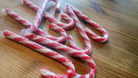 shiny plastic wrapped striped christmas candy canes on wooden kitchen table home decoration rotating left