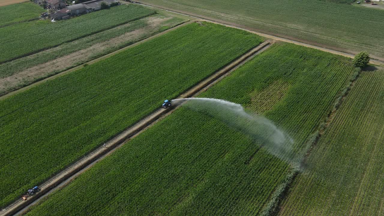 4K drone aerial footage starting from a near top-down view above a water sprinkler, rotating counterclockwise and moving backward with a gimbal tilt-up revealing a lush green farmland in Italy