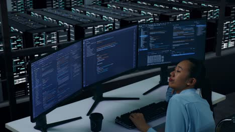 vista lateral de una mujer asiática aburrida desarrollador escribir código con múltiples pantallas de computadora en el centro de datos