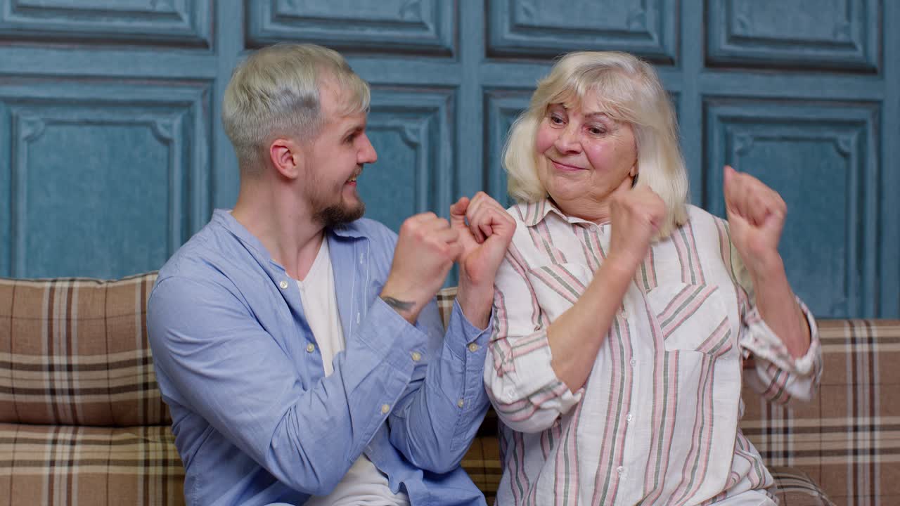 한 세대의 고령 어머니와 잘생긴 성인 아들 또는 손자의 가족이 함께 춤추고 웃고 있습니다.